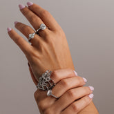 Hand wearing multiple 18k gold rings on a neutral background